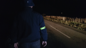 Pieszy z opaska na rekawie idzie poboczem drogi w nocy