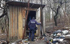 Policjant w mundurze idzie w kierunku altanki działkowej, dookoła są pozostałości śniegu na ziemi. Zdjęcie zboone na działkach w porze dziennej.