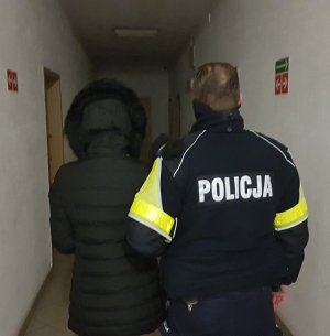 policjant umundurowany prowadzi zatrzymaną do sprawy kobietę.Zdjęcie wykonane na korytarzu komendy