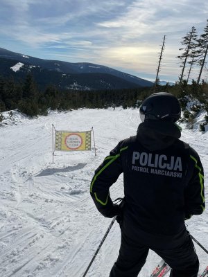 Policjant na nartach znajduje sie na stoku narciarskim . Dookoła leży śnieg