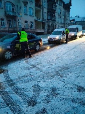 dwóch policjantów stoi przy samochodach znajdujących sie na ulicy