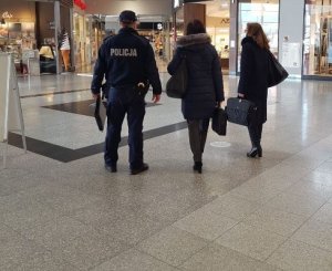 Policjant z dwiema pracownicami sanepidu na kontroli w galerii handlowej. Stoją na głównym holu pomiędzy sklepami.