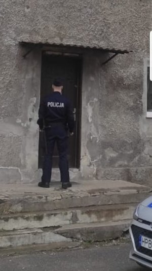 Policjant umundurowany stoi przed wejściem do budynku