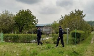 patrol policji idzie przez teren ogródków działkowych.Policjanci maja na twarzach maseczki w tle widać krzaki