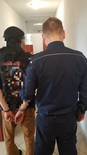 policjant  umundurowany prowadzi zatrzymanego, który ma założone na rękach kajdanki