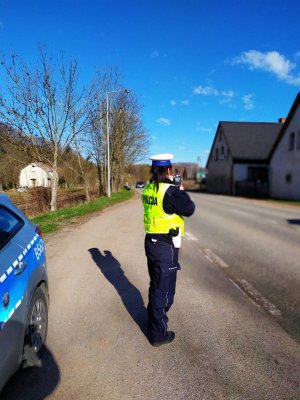 Policjantka stoi z miernikiem prędkości na drodze , na poboczu jest zaparkowany radiowóz