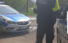 policjant nadzoruje ruch drogowy na drodze , w pobliżu zaparkowany przy drodze radiowóz policyjny oznakowany