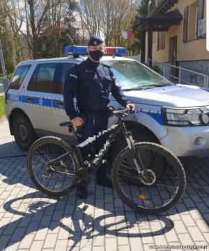 policjant stoi przy radiowozie i trzyma odzyskany rower