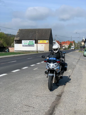 policjant  siedzi na motocyklu  służbowym w tle widać drogę i budynek