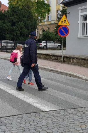 Policjant przeprowadza przez ulice dwoje dzieci w rejonie szkoły